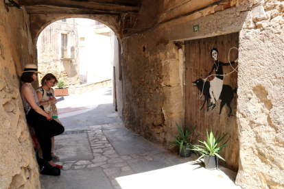 Una de las artistas participantes en la edición 2018 del concurso Riu d'Art de Riba-roja d'Ebre conversando delante de una de las puertas que ha pintado con dibujos inspirado en historias locales.