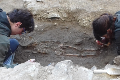 Los restos del esqueleto de niño encontrado en Romanyà con dos de las arqueólogas trabajando.