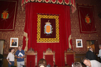 Pla general del saló de plens, amb l'escut municipal presidint-lo, la foto de Quim Torra a l'esquerra i la de Felip VI a la dreta de la imatge.