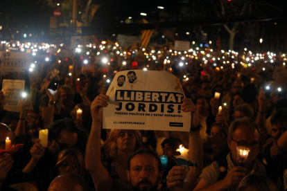 Un home sosté una pancarta de 'Llibertat Jordis' i, al seu voltant, persones amb espelmes enceses.