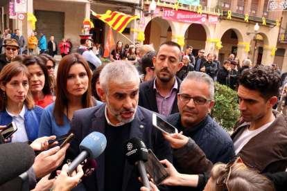 El portavoz parlamentario de Ciudadanos, Carlos Carrizosa, atendiendo los medios de comunicación, mientras detrás hay un grupo de personas protestando, en una visita a Valls.