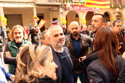 El portavoz parlamentario de Ciutadans, Carlos Carrizosa, sonriendo en medio de una multitud en Valls, mientras detrás hay un grupo de personas protestando, en una visita la capital del Alt Camp.