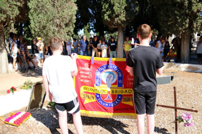 Dos joves familiars dels brigadistes britànics portant una bandera de l'entitat IBMT durant l'homenatge a la fossa comuna del cementiri del Perelló.