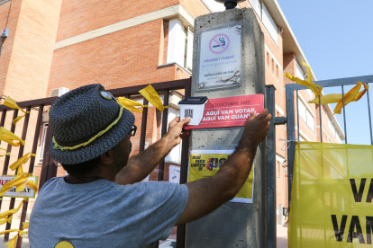 Un home penja un cartell que reivindica l'1 d'octubre  a la porta de l'Institut Comte de Rius.