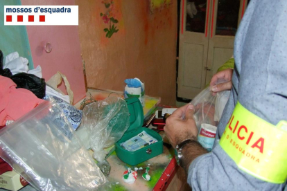Un agent dels Mossos d'Esquadra inspeccionant les drogues i altres efectes intervinguts en un pis de Roquetes.