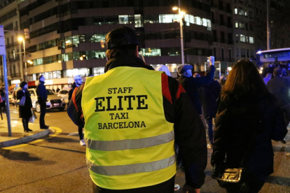 Un taxista d'esquenes amb una armilla groga de l'associació Èlite Taxi a la concentració de taxistes a la cruïlla de passeig de Gràcia amb el carrer Aragó.