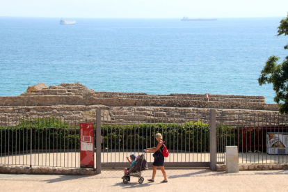 Plan|Plano general de una mujer pasando con el carret de un bebé por delante de la reja del anfiteatro romano de Tarragona, cerrado al público de forma provisional. Imagen del 27 de septiembre del 2019