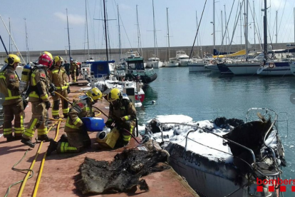 Bombers actuant al port de Torredembarra davant l'embarcació que ha cremat.