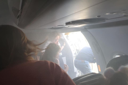 Diversos passatgers sortint de l'avió, plena de fum.