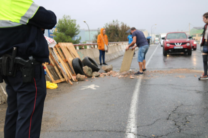 Corte en la carretera N-240 en Valls, junto al polígono industrial, de jóvenes dejando escombros en la calzada ante una cola de coches y las piernas de un mosso en primer término.
