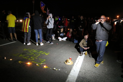 Algunos manifestantes cantando al sonido de la gralla ante los escritos y las velas que han dejado en la N-340 en Amposta.
