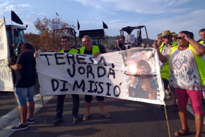 Pla general d'un grup de manifestants afectats pels focs del juny mostrant una pancarta que demana la dimissió de la consellera Teresa Jordà, el 18 d'agost del 2019 (horitzontal)