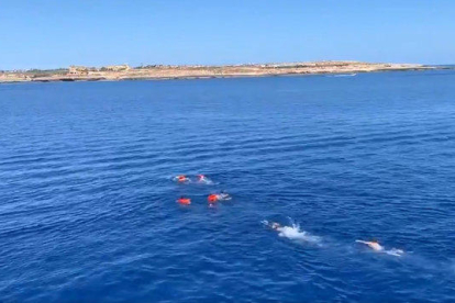 Cuatro rescatados por el Open Arms se tiran en el agua y son perseguidos por socorristas, con la costa de Lampedusa al fondo.