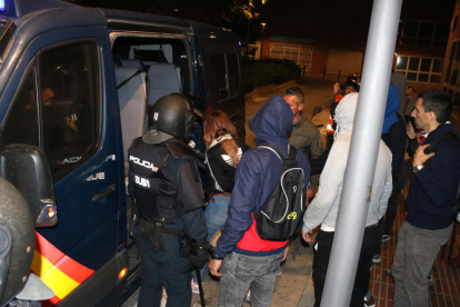 Pla general de la noia detinguda pujant a la furgoneta de la Policia Nacional, envoltada d'agents.