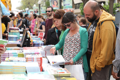 Diverses persones fullegen llibres durant la Diada de Sant Jordi a la Rambla Nova de Tarragona.
