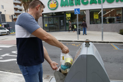 Imagen de un hombre tirando una bolsa de basura en el contenedor de resto o rechazo en una isla de contenedores al centro de Valls
