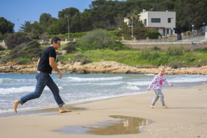 Un pare jugant i corrent amb la seva filla per la sorra de la platja de l'Arrabassada, espai escollit per moltes famílies per passejar i sortir una estona.