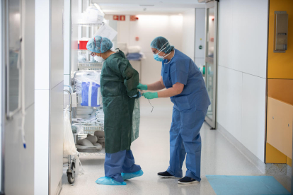 Una professional sanitària corda a una companya una bata abans d'atendre un pacient amb covid-19, en un dels blocs quirúrgics de l'Hospital Clínic de Barcelona habilitat com a UCI en la pandèmia de coronavirus.