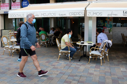 La terraza de una cafetería en Calafell Platja mientras un hombre pasea con mascarilla