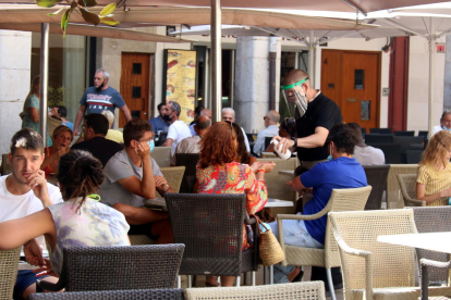 Un camarero de una terraza de la plaza del Ayuntamiento poniendo hidrogel a unos clientes.