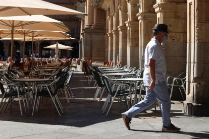 Un hombre con mascarilla pasa frente a una terraza de un restaurante de la plaza Mayor de Salamanca.