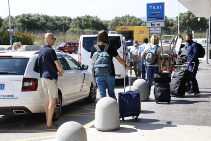 Pla general de turistes amb maletes, esperant agafar un taxi a l'aeroport de Reus, després d'aterrar amb el primer avió que arriba a la capital del Baix Camp des de l'alarma, provinent del Regne Unit.