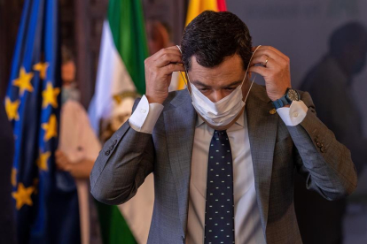 El presidente de la Junta de Andalucía, Juanma Moreno, se coloca una máscara después de anunciar hoy en Sevilla