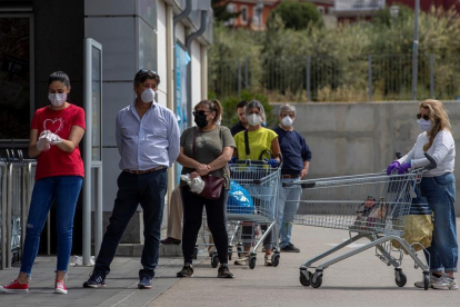 Diverses persones protegides amb mascaretes fan cua en l'entrada d'un supermercat.