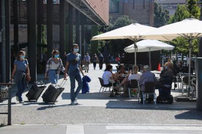 Uns turistes amb mascareta passant davant d'una terrassa amb diverses persones prenent un refresc amb mascareta aquest dissabte 18 de juliol de 2020 a Figueres.