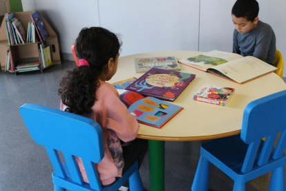 Imagen de dos niños disfrutando de libros en la nueva biblioteca infantil de las urgencias pediátricas del Hospital Joan XXIII.