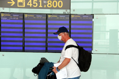 Imatge d'un viatger amb mascareta passant per davant dels panells informatius sense cap vol el 18 de març de 2020.