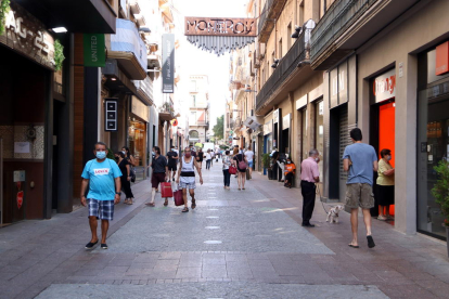 Plano general de varias personas con bolsas de compra en la calle Monterols de Reus.