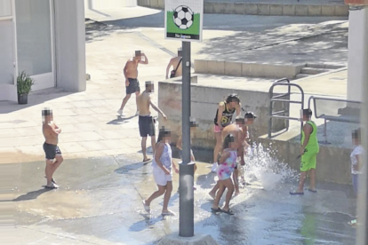 Un grupo se refresca con el agua a presión, en una plaza del barrio.