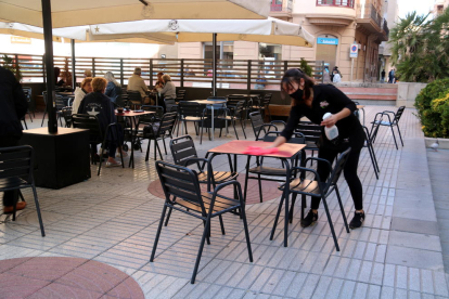 Una cambrera netejant una taula en la terrassa mig buida d'una cafeteria de Tortosa.