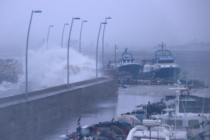 Una gran onada batent contra el moll del port de l'Ampolla amb les barques de pesca amarrades a l'interior.
