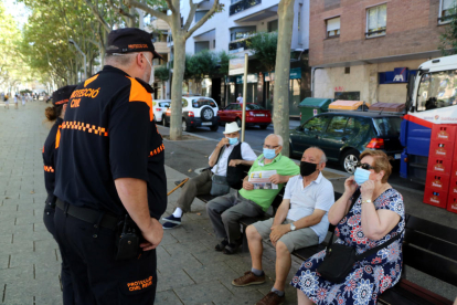 Dos voluntaris de Protecció Civil controlant l'ús de mascareta entre diversos veïns de Reus asseguts en un banc al passeig Sunyer.
