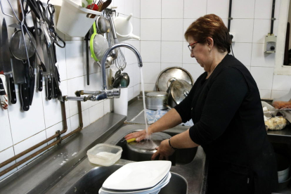 Pla general d'una dona de Castellolí mentre frega els plats amb l'aigua de l'aixeta.