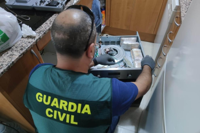 Un agente de la Guardia Civil confiscando fajos de billetes escondidos en la cocina de un piso.