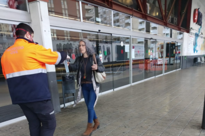 Un miembro de Protección Civil dando una mascarilla a una usuaria a la estación de autobuses de Tarragona.
