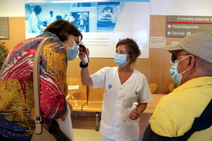 Pla mitjà d'una infermera prenent la temperatura a dos pacients abans que entrin a consultes externes de l'Hospital Verge de la Cinta de Tortosa.