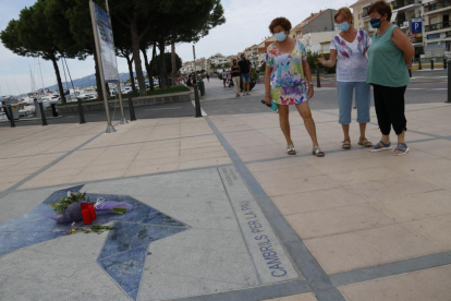 Tres mujeres observando unas flores y unas velas sobre el memorial conmemorativo de los atentados terroristas, ante|delante de el Club Náutico de Cambrils.
