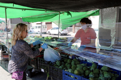 Una clienta del mercat de Sant Salvador de Tarragona recollint una bossa de la compra de la parada de fruita i verdura, protegida amb film transparent.