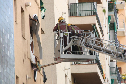 Dos bombers dalt d'una grua elevadora davant una finestra destrossada del pis sinistrat a Premià de Mar