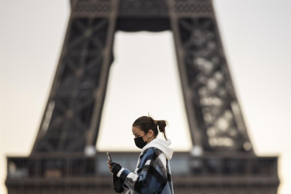 Una mujer con mascarilla pasando delante de la Torre Eiffel.