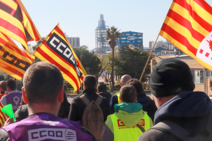Trabajadores camino de la puerta de IQOXE, durante la huelga en el sector petroquímico de Tarragona, con la empresa en el fondo.