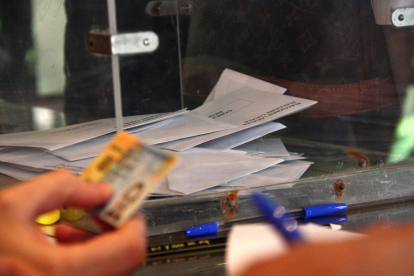 Foto de archivo de una urna y una mano que comprueba el DNI para poder votar.