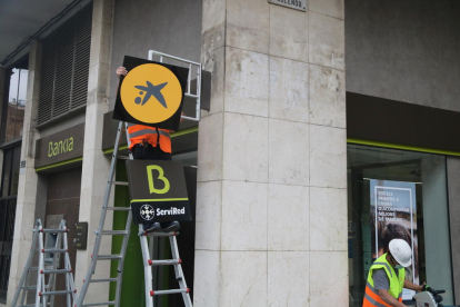 Un operari canviant el logotip de Bankia pel de CaixaBank en una oficina.