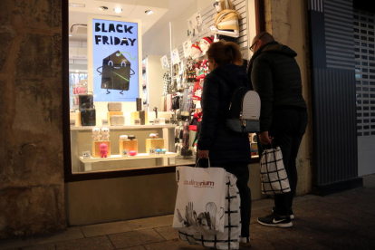 Dos compradors amb bosses de comprar mirant un aparador d'una botiga del centre de Reus, en el primer cap de setmana de la campanya de Nadal