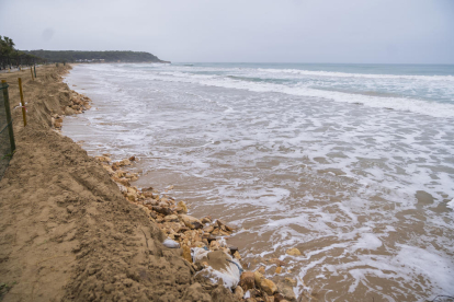Imagen de la playa Larga, totalmente tragada por|para el agua del mar y con las rocas y las sacas del muro del camping caído.