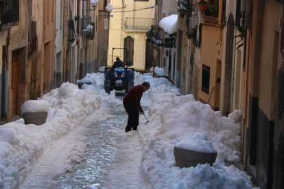 Un carrer de Falset nevat amb un veí retirant neu de la porta de casa seva i un tractor netejant.